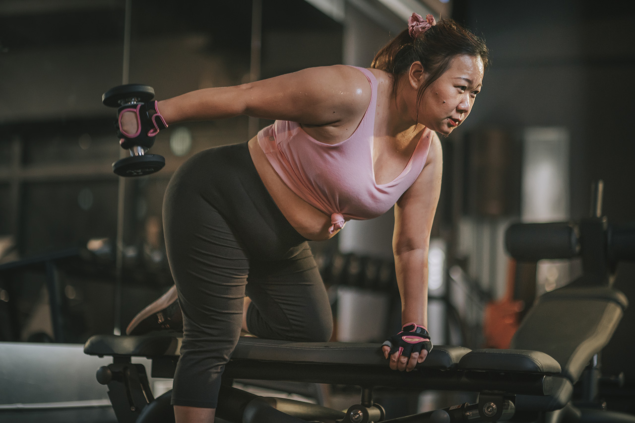 body-positive-Asian-mid-adult-woman-exercising-with-dumbbells-in-a-lunge-position-at-gym-bench-at-night-1332406157_6048x4024_1280px